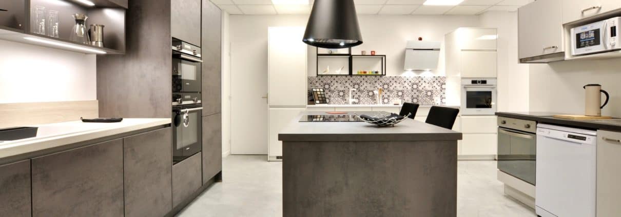 Façade et plan de travail en décor béton gris ardoise, électroménager Siemens, hotte suspendue Elica. A droite, linéaire promotion immobilière avec façades en finition gris soie, électroménager Candy, évier et robinetterie Blanco.