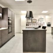 Façade et plan de travail en décor béton gris ardoise, électroménager Siemens, hotte suspendue Elica. A droite, linéaire promotion immobilière avec façades en finition gris soie, électroménager Candy, évier et robinetterie Blanco.