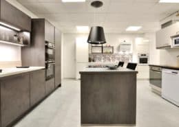 Façade et plan de travail en décor béton gris ardoise, électroménager Siemens, hotte suspendue Elica. A droite, linéaire promotion immobilière avec façades en finition gris soie, électroménager Candy, évier et robinetterie Blanco.