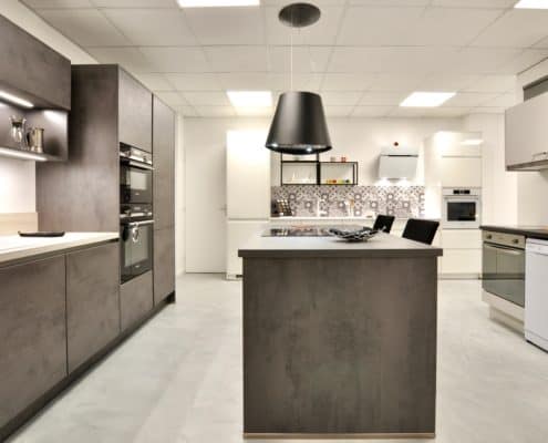 Façade et plan de travail en décor béton gris ardoise, électroménager Siemens, hotte suspendue Elica. A droite, linéaire promotion immobilière avec façades en finition gris soie, électroménager Candy, évier et robinetterie Blanco.